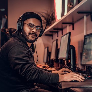 A young African American guy, enjoying spending time with his friends, playing in a multiplayer video game on a PC in a gaming club or internet cafe. APC by Schneider Electric patrocina la mayor competición eSport multiplataforma en Latinoamérica