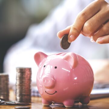 businessman-holding-a-coin-in-a-piggy-bank-on-a-ta-2026-03-20-00-33-43-utc ¿Cuáles son los 5 hábitos para mejorar los ahorros en la segunda mitad del año?